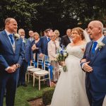 Bride walks down aisle with father at outdoor wedding.