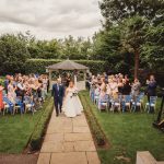 Bride and groom walking down garden aisle.