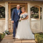 Bride and groom pose in garden gazebo.