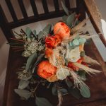 Orange and white floral bouquet on wooden chair.