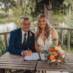 Wedding couple signing certificate by lakeside gazebo.