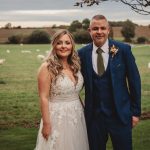 Bride and groom in countryside with sheep grazing.