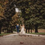 Bride and groom walking under tree-lined path.