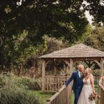 Wedding couple by wooden gazebo in lush garden.