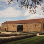 Historic stone barn with landscaped gardens under cloudy sky.