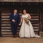 Bride and groom standing by wooden barn.