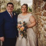 Happy couple posing in wedding attire with flowers.